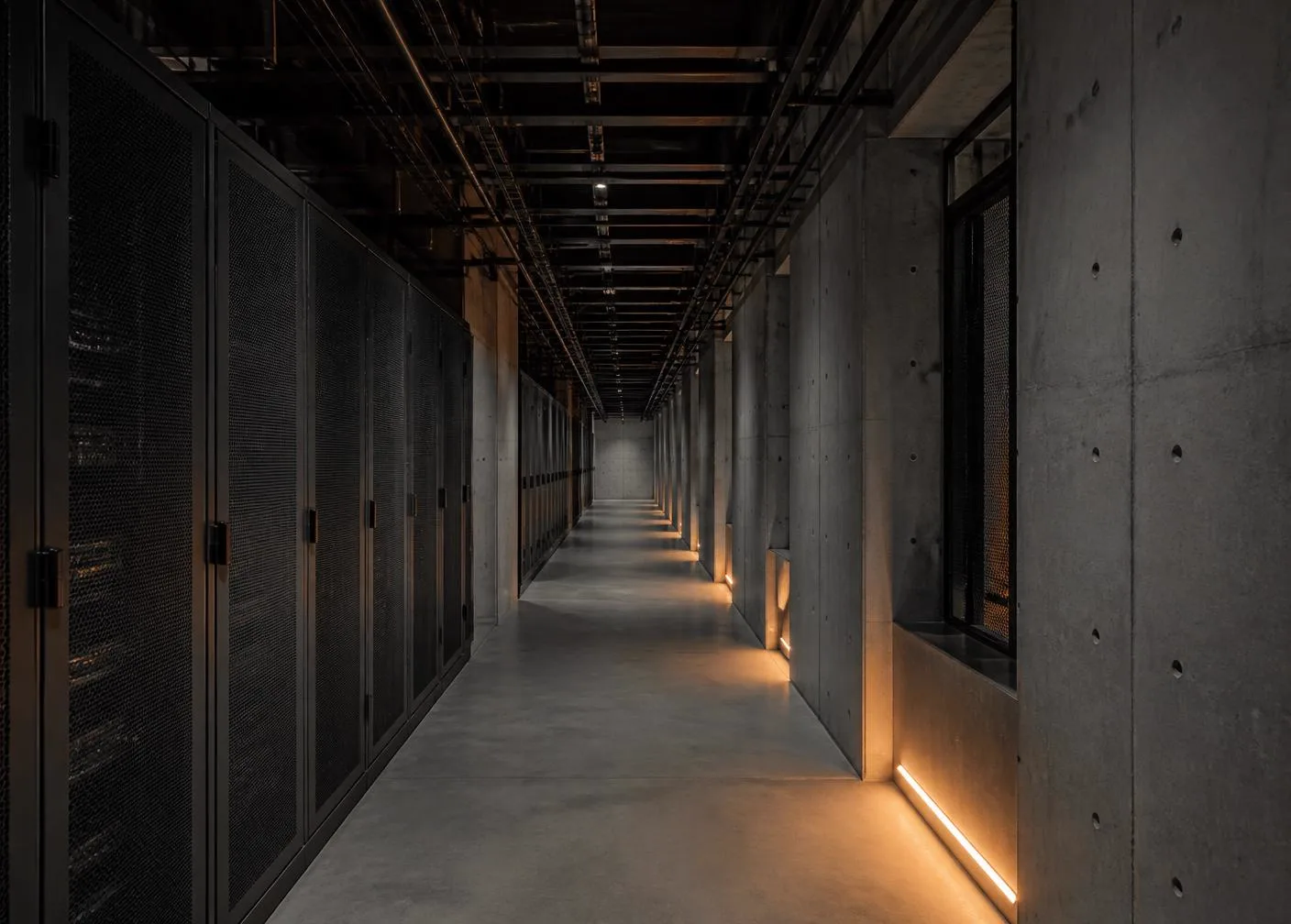Corridor of dark server cabinets in a cloud data centre lit by low amber floor lighting